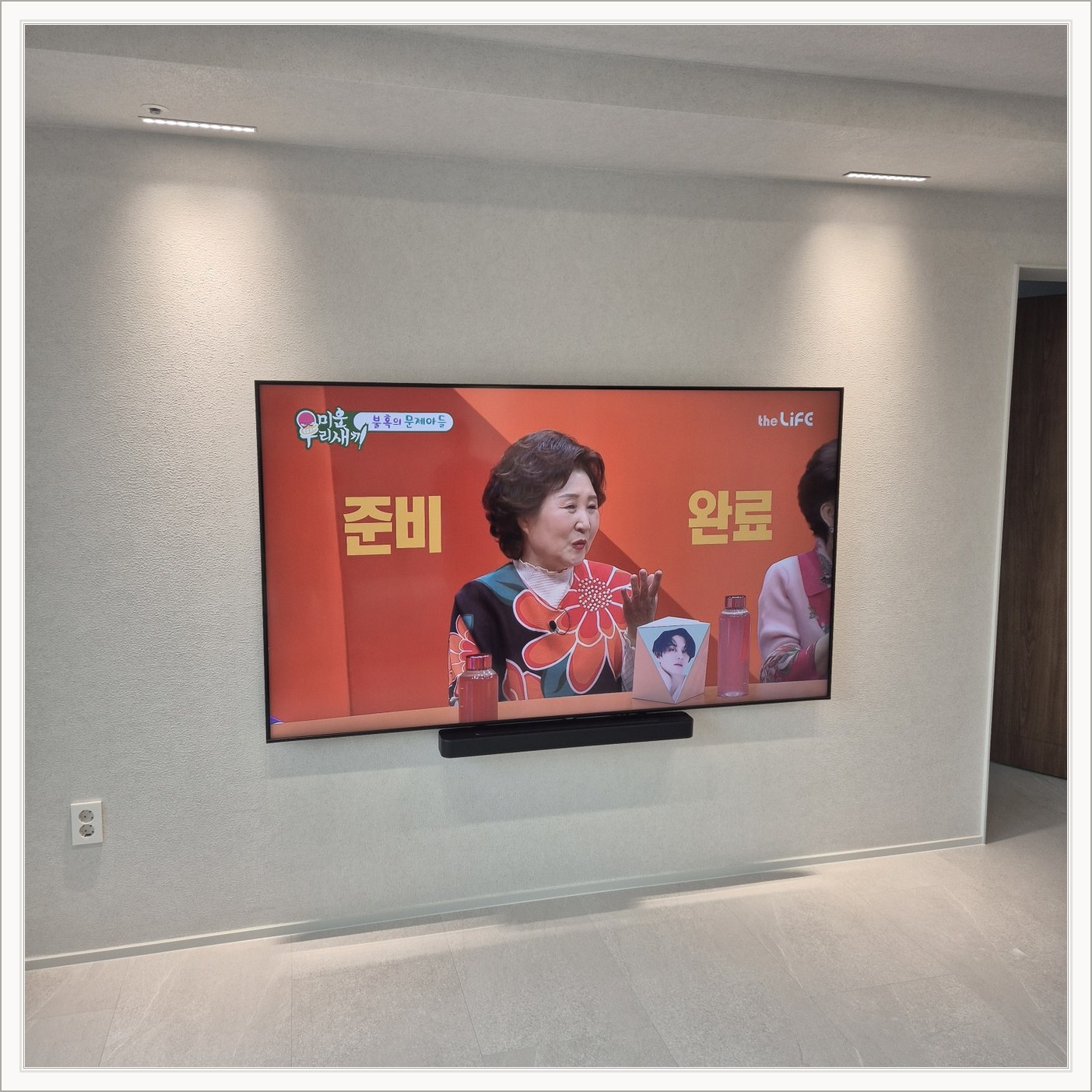 조명이 비추는 미색 벽과 사운드바 — 사운드바와 벽면의 간격이 한눈에 들어옵니다
