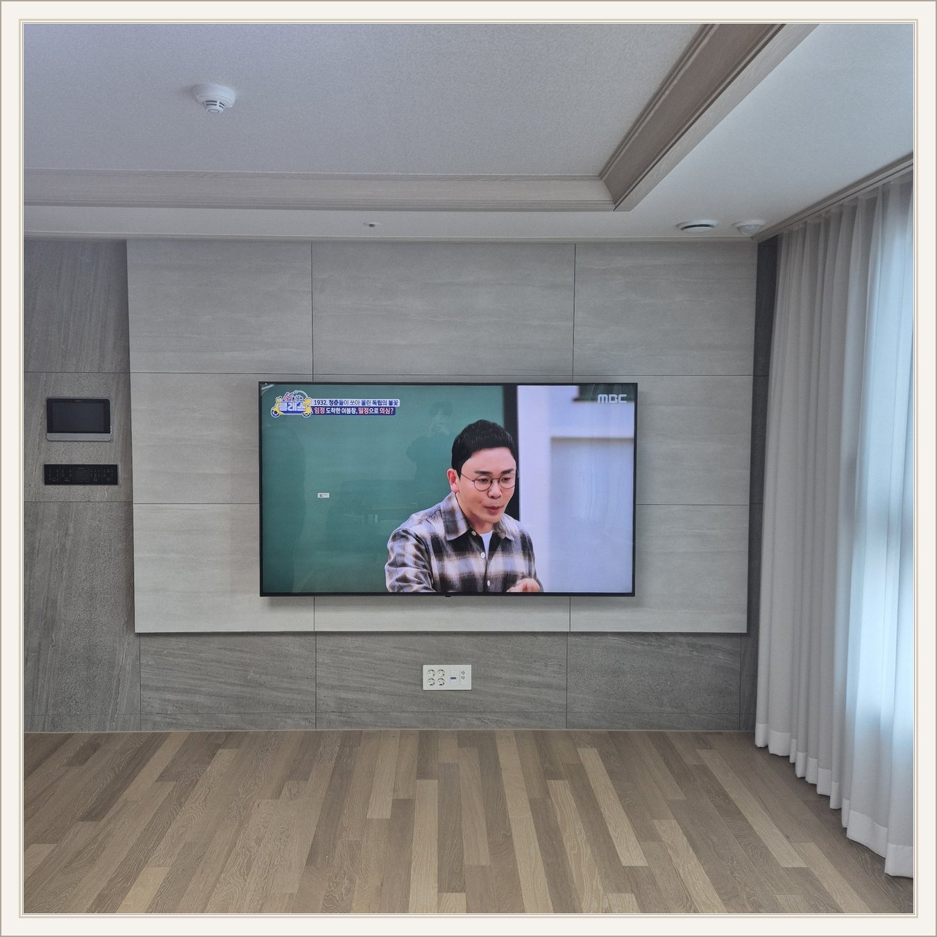 거실 회색 패널과 벽걸이 TV — TV 아래 콘센트와 양쪽 마감 판넬의 대비가 뚜렷합니다