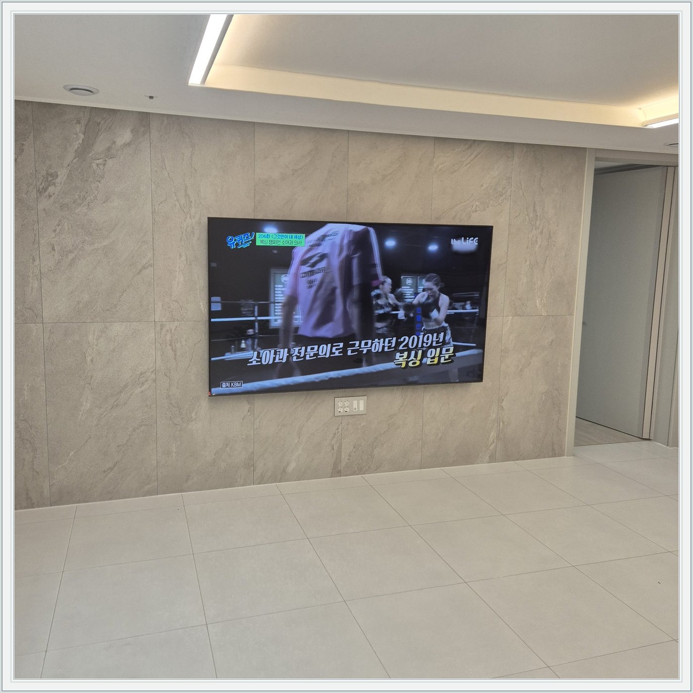 석재 느낌 벽면을 정면에서 본 TV — 벽 마감의 세로 이음선이 TV 양옆에 남아 있습니다