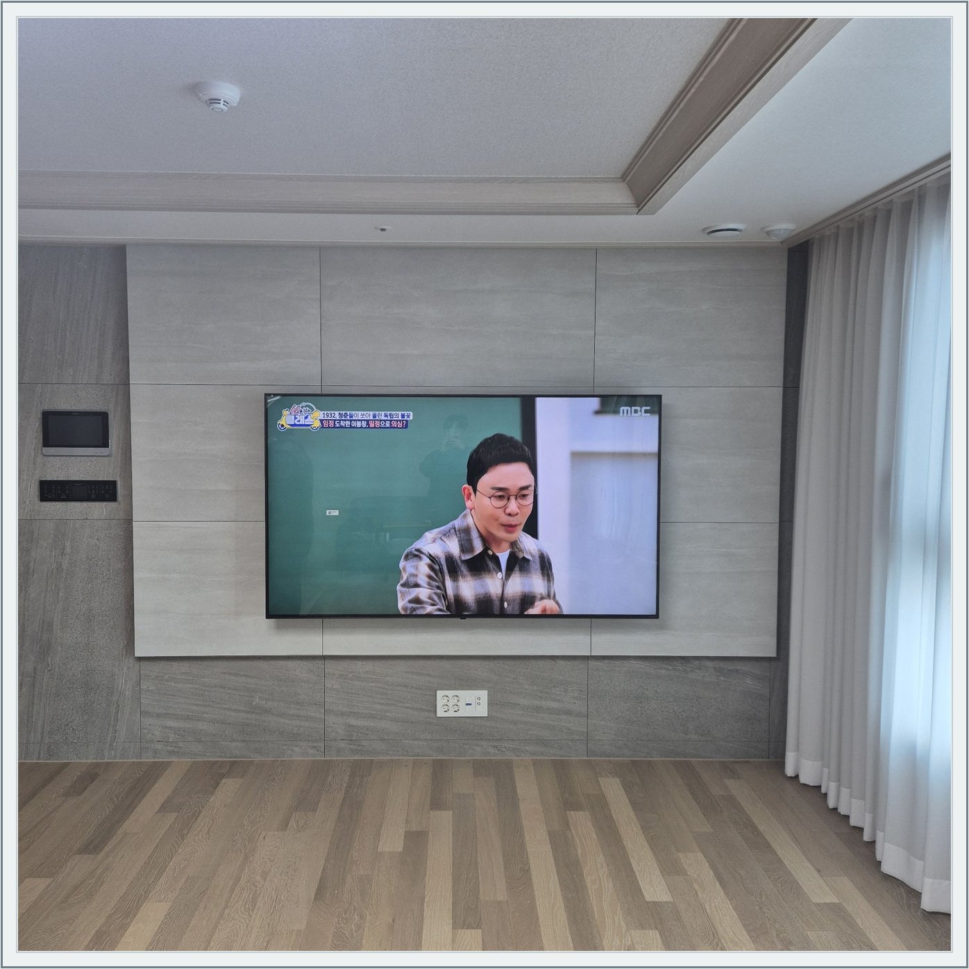 거실 회색 패널과 벽걸이 TV — TV 아래 콘센트와 양쪽 마감 판넬의 대비가 뚜렷합니다