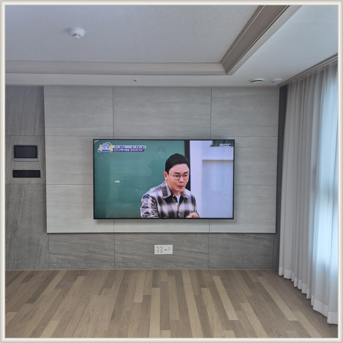 거실 회색 패널과 벽걸이 TV — TV 아래 콘센트와 양쪽 마감 판넬의 대비가 뚜렷합니다
