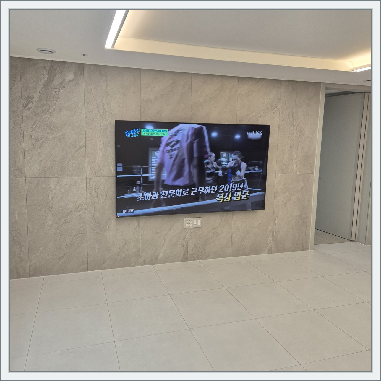 석재 느낌 벽면을 정면에서 본 TV — 벽 마감의 세로 이음선이 TV 양옆에 남아 있습니다