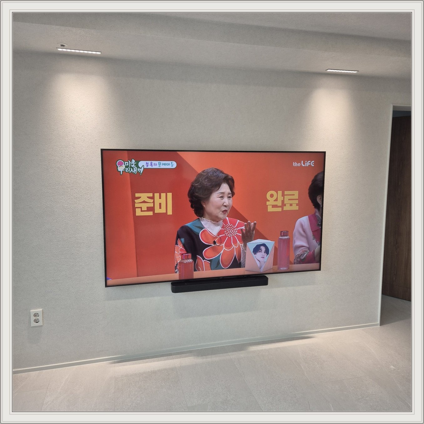 조명이 비추는 미색 벽과 사운드바 — 사운드바와 벽면의 간격이 한눈에 들어옵니다